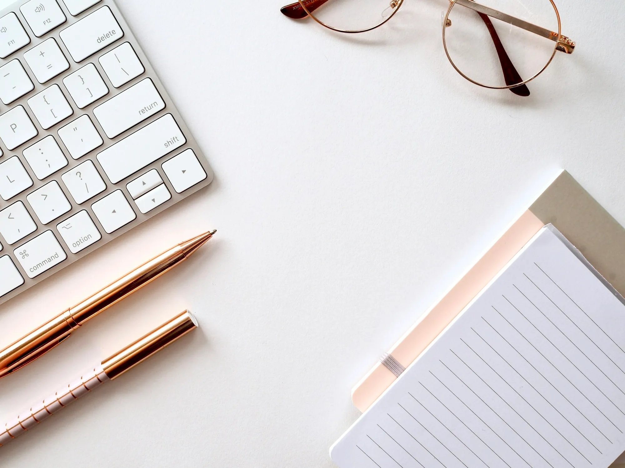 A minimal desk seen from above with a notebook, pen and laptop